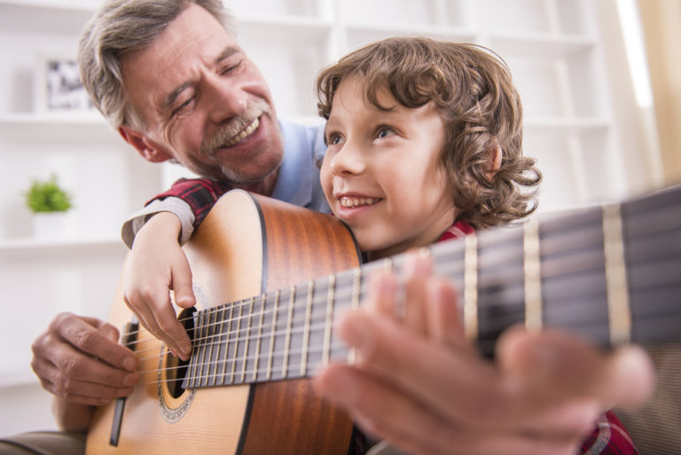 niño aprendiendo a tocar la guitarra con su abuelo