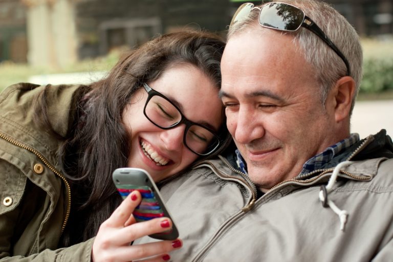 Hija sonriente enseñando a su padre algo en el móvil
