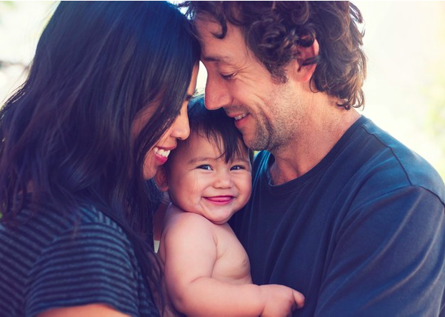 madre y padre abrazando a su hijo bebé que sonrie