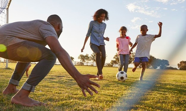 padre y madre jugando futbol con sus hijos