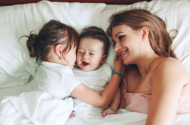 niña pequeña dandole un beso a su hermano bebe y su mamá viendolos sonriendo