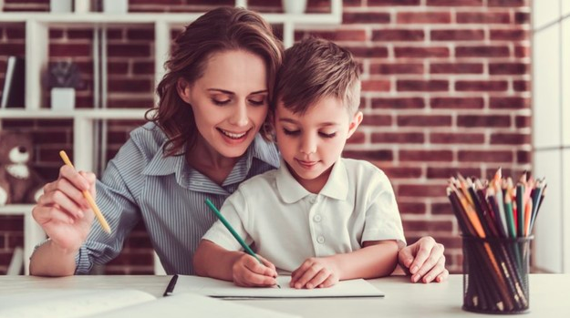 niño aprendiendo a escribir ayudado por su mamá