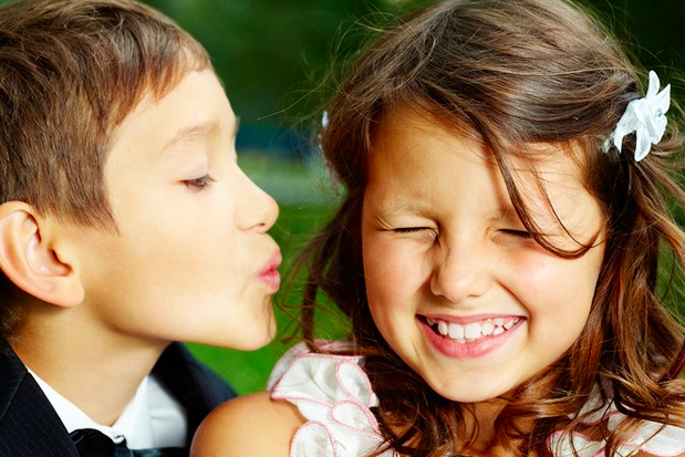 niño con gesto de beso en la mejilla hacia una niña