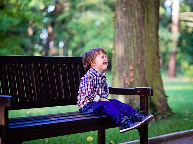 niño sentado en una banca de un parque haciendo berrinche