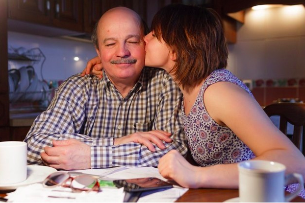 Hija mayor dandole un beso a su padre anciano