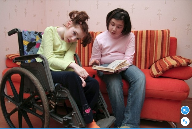 niña leyendo un libro junto a otra niña en silla de ruedas