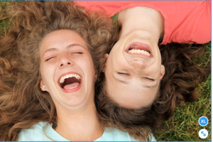 2 mujeres jovenes sonriendo acostadas en el pasto viendo el cielo
