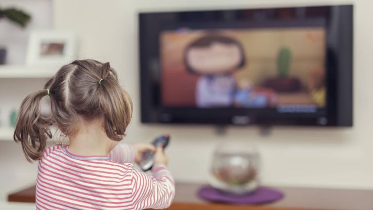 Niña usando un control de televisor viendo un programa de dibujos animados