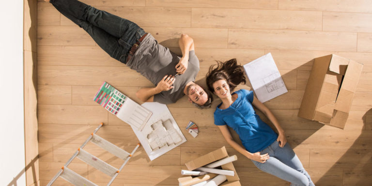 esposos en una sala vacia con cajas y escaleras y colores viendo el techo