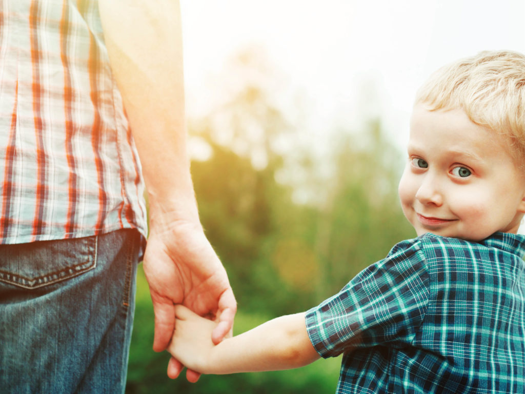 niño alegre tomado de la mano por su padre