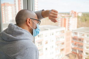 Hombre solitario en máscara médica mirando por la ventana. Aislamiento en casa para auto cuarentena. Concepto de cuarentena domiciliaria, prevención COVID-19. Situación del brote de coronavirus