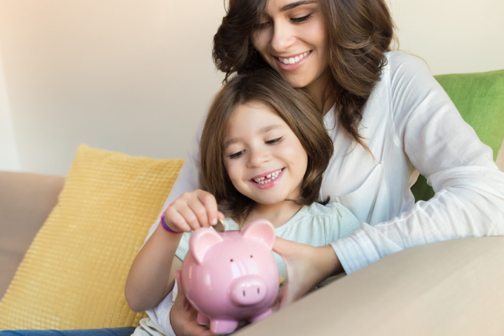 Mujer enseñándole a su hija ahorrar colocando una moneda en una alcancía