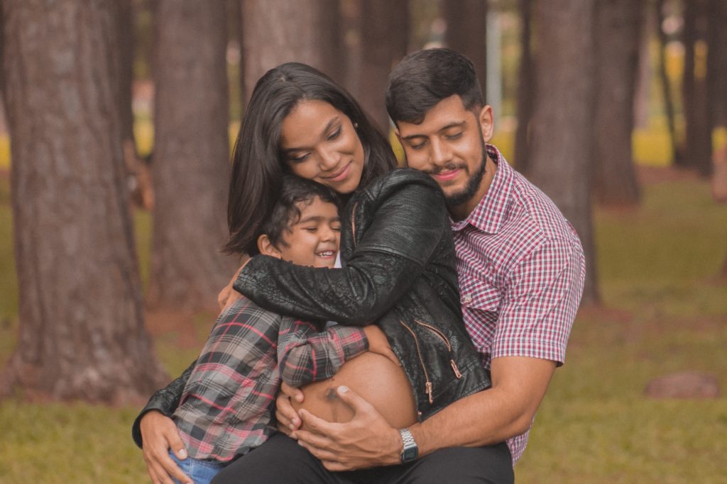 Mujer embarazada siedo abrazada por su esposo e hijo en un parque