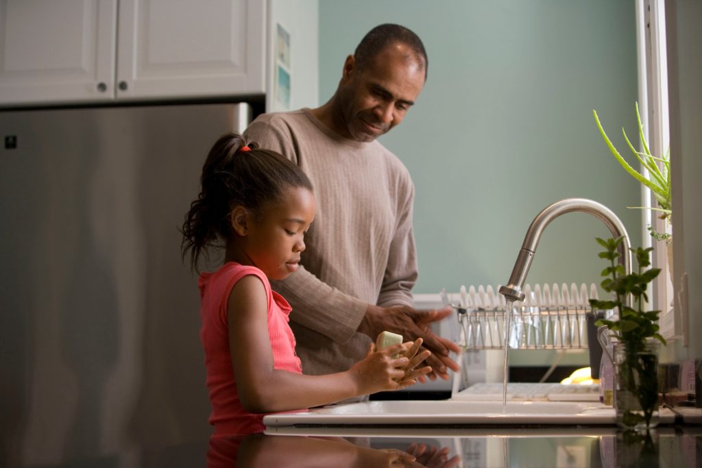 Hombre enseñandole a su hija a lavar los platos