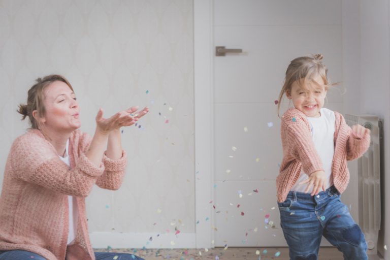 Mamá soplando pedacitos de papel de colores a su hija que sonrie