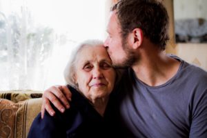 Hijo adulto dandole un beso a su mamá mayor sentados en el sillon