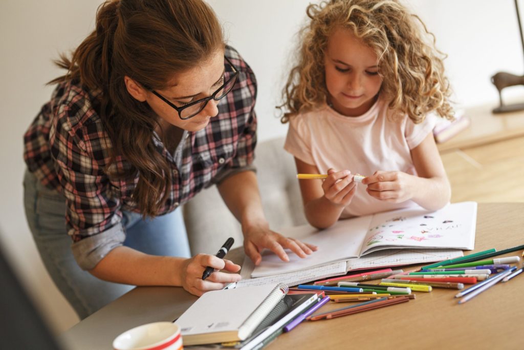 Hija dibujando en un cuaderno y mamá ayudandole