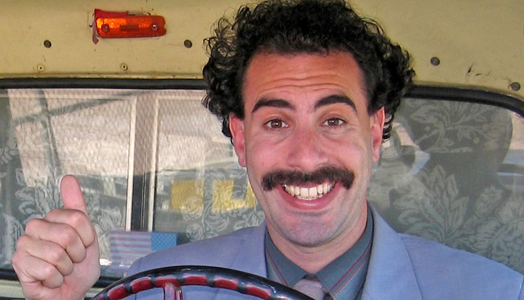 Un hombre con bigote sonriente manejando una camioneta, Escena de la pelicula BORAT 2 SUBSEQUENT MOVIE FILM