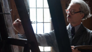 hombre blanco con bigote con aire de intelectual escribiendo en un vidrio, Escena de pelicula THE LAST VERMEER