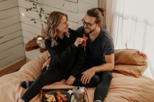 Pareja joven comiendo en la cama y riendo