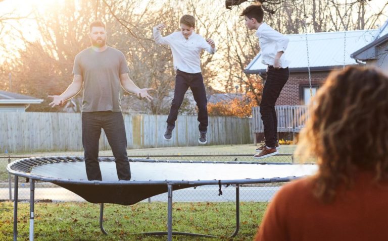 Niños jugando en un trampolin junto al padre que mira a su esposa en forma de interrogación miestra ellas lo ve de lejos a los 3