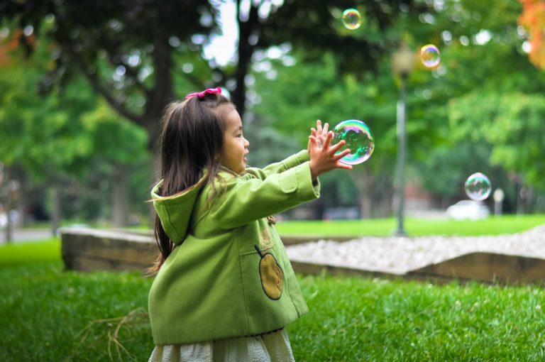 Niña jugando con burbujas de jabon en el zacate verde de un parque