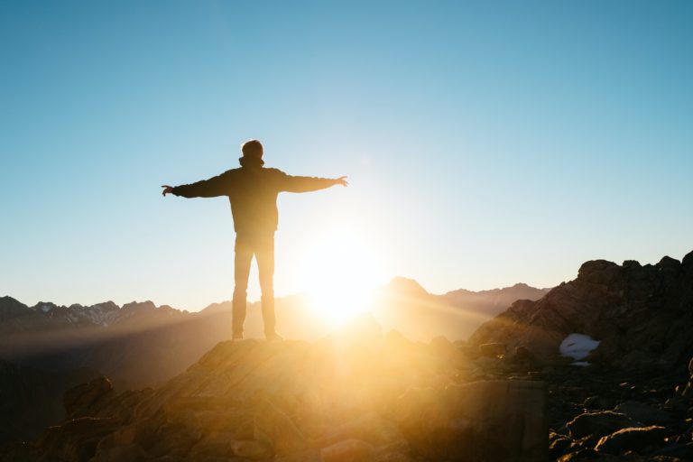 Foto de persona en una colina con brazos abiertos con la luz del atardecer frente a ella