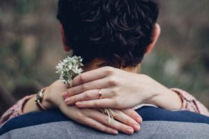 Manos de una prometida alrededor de su prometido con unas flores en las manos