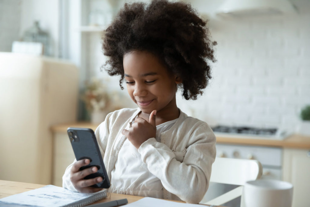 Niña joven Afrodescendiente con cabello colocho viendo un celular en la cocina