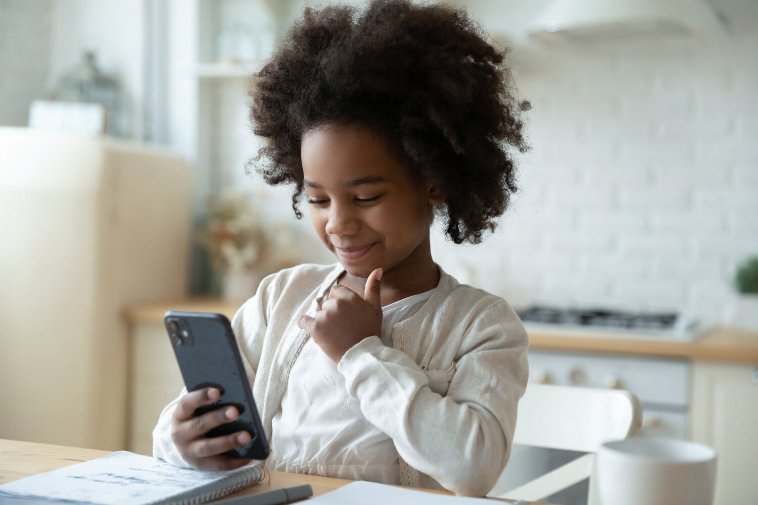 Niña joven Afrodescendiente con cabello colocho viendo un celular en la cocina