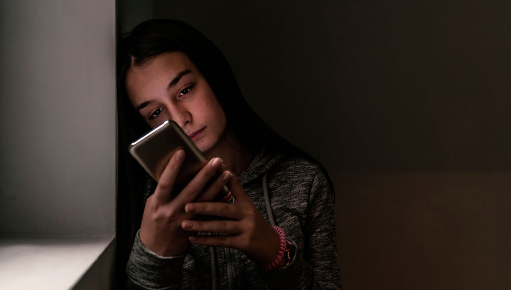 Mujer triste apoyada en la pared viendo su celular