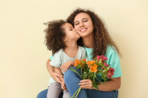Mamá colocha con flores abrazando a su hijo con colochos que le está dando un beso