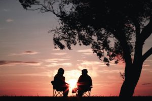 Silueta de una pareja sentados bajo un árbol viendo un atardecer