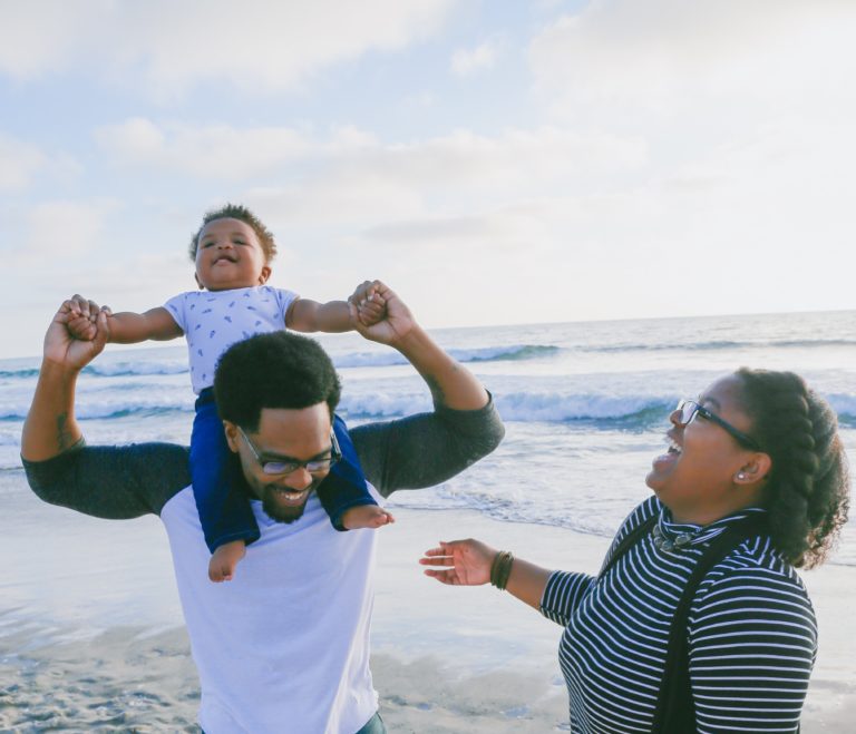 Papá y mamá afrodescendientes jugando con su hijo en la playa alegres