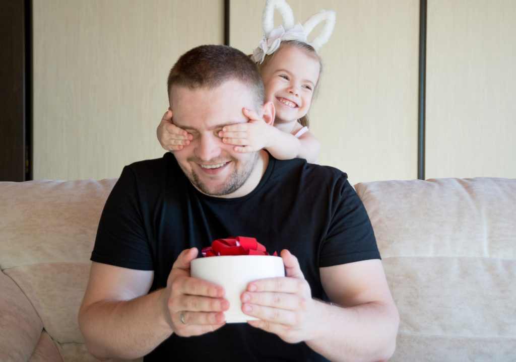 niña tapando los ojos de su padre que tiene un regalo en sus manos