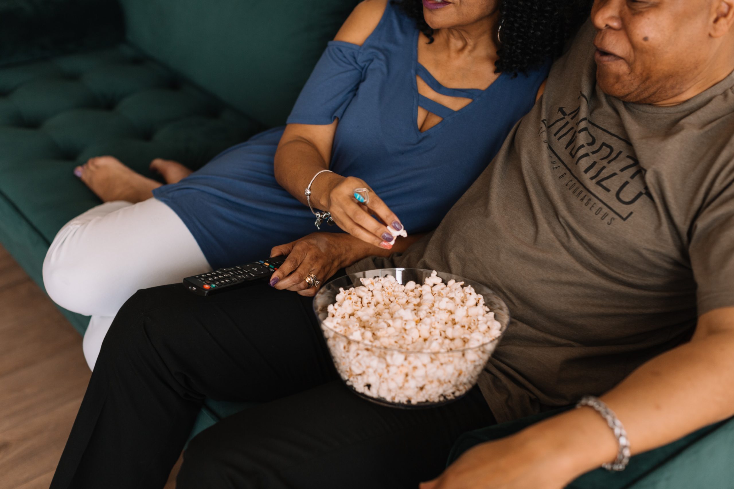 Esposos en un sillon viendo televisión y comiendo palomitas de maiz