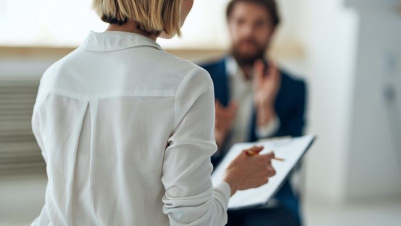 Mujer tomando apuntes y hablando con un hombre en un acita de consejería