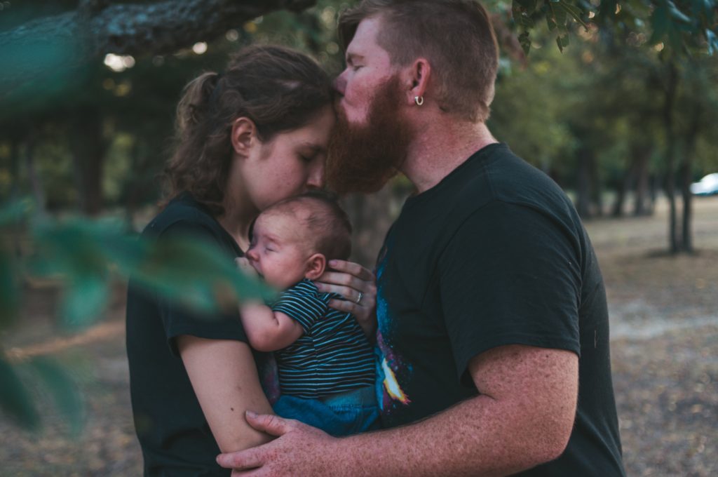 Padre besando a su esposa que abraza a su bebé en brazos